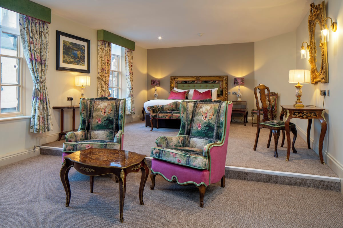 A hotel room with a bed, two armchairs, a table, and a mirror.