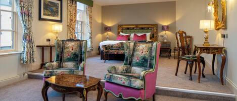 A hotel room with a bed, two armchairs, a table, and a mirror.