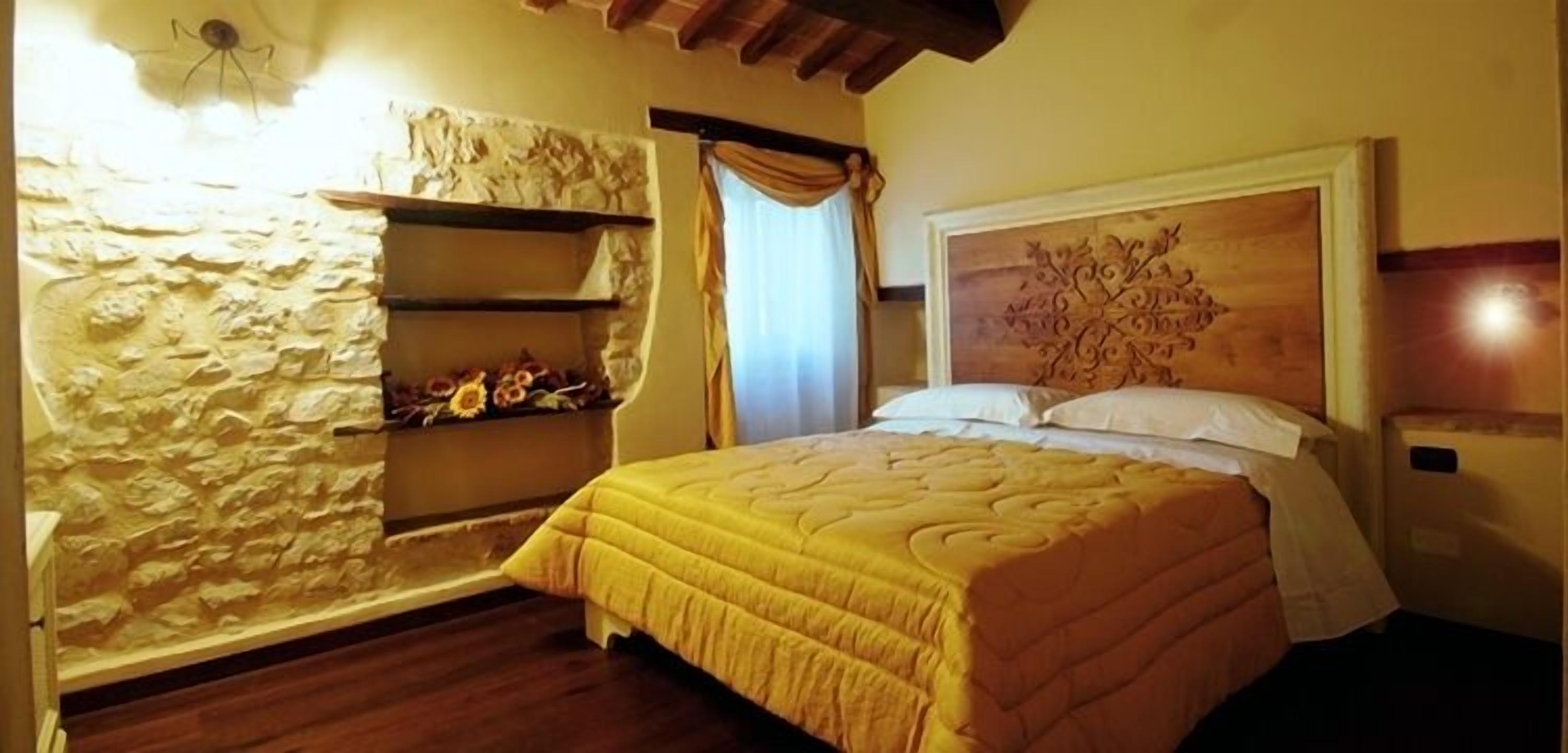 A bedroom with a stone wall, a wooden headboard, and a bed with a yellow bedspread.
