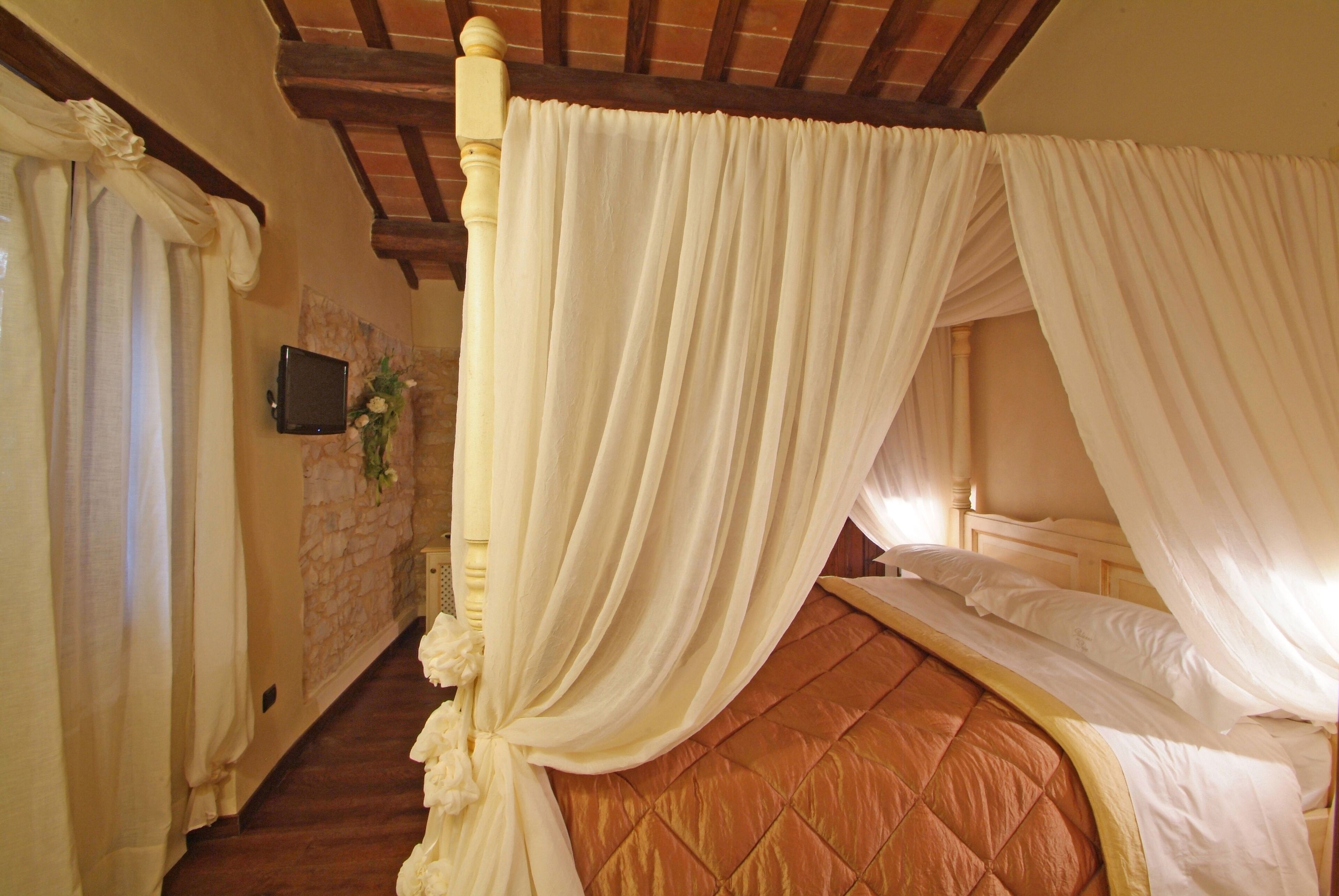 A bedroom with a four-poster bed, a stone wall, and a television mounted on the wall.