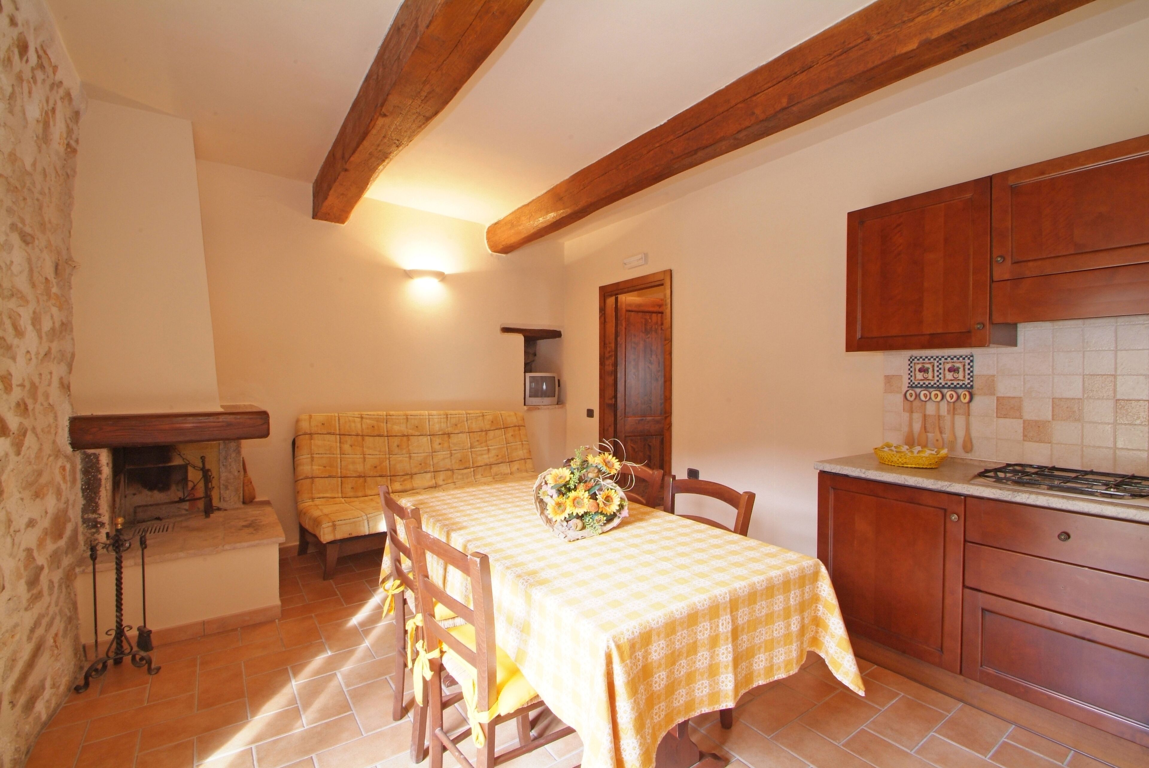 Un comedor acogedor con mantel a cuadros, sillas de madera y un banco. Una cesta de flores añade un toque de color.