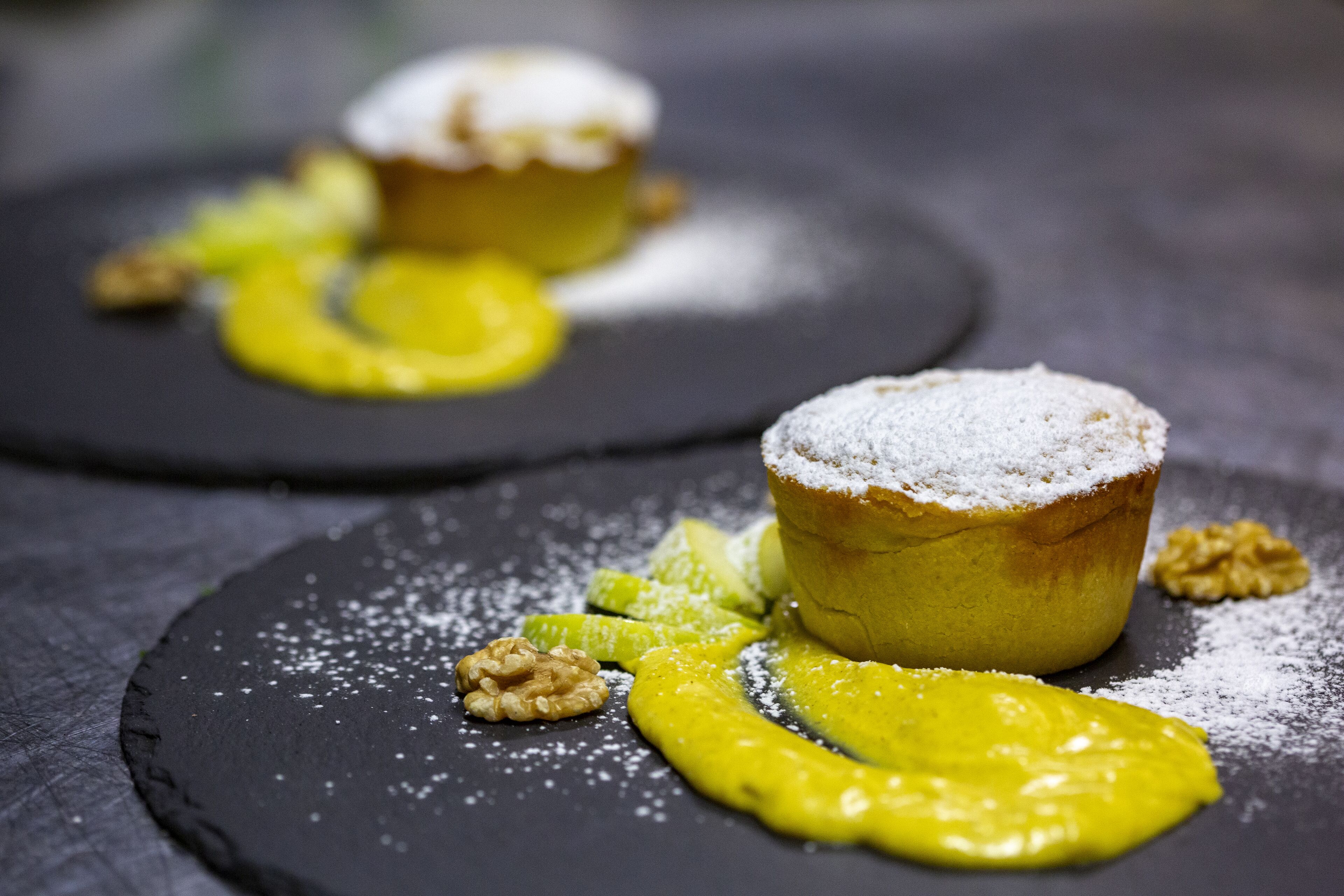 A dessert with a pastry on a slate plate, accompanied by a yellow sauce and walnuts.