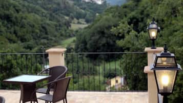 Una terrazza con tavolo e sedie, una ringhiera e due lanterne illuminate.