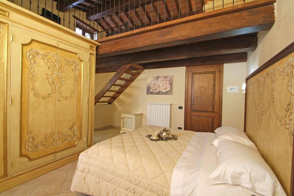 A bedroom with a large bed, a wooden wardrobe, a staircase, and a radiator.