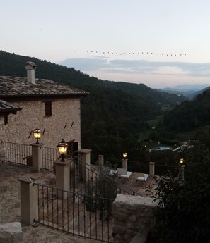 A stone building with a tiled roof, a balcony with a railing, and a view of a valley with trees and distant mountains. - Palazzo del Papa Agriturismo (Spoleto)