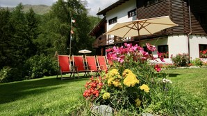 A wooden chalet with a balcony, surrounded by a well-maintained garden with colorful flowers and a red chair set. - Villa Anna Maria (Ayas)