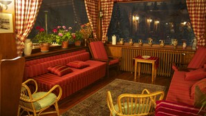 A cozy room with a red sofa, two wicker chairs, a small table, and a window with checkered curtains. - Villa Anna Maria (Ayas)