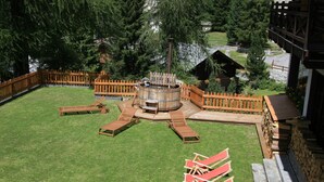 A hot tub surrounded by wooden deck chairs and a wooden fence. - Villa Anna Maria (Ayas)
