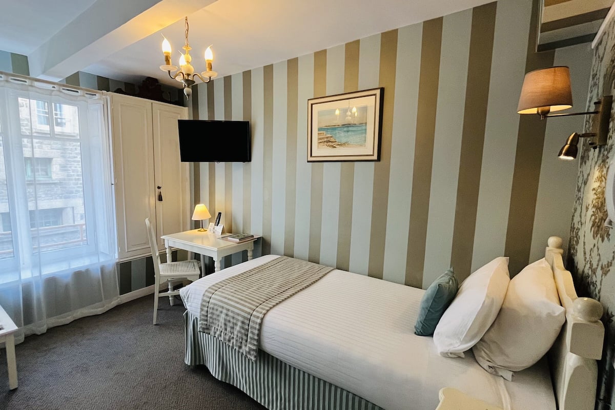 A hotel room with a bed, a desk, a chair, a TV, and a window with curtains.