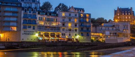 Et hotel ved vandet med flere etager, balkoner og oplyst skiltning.