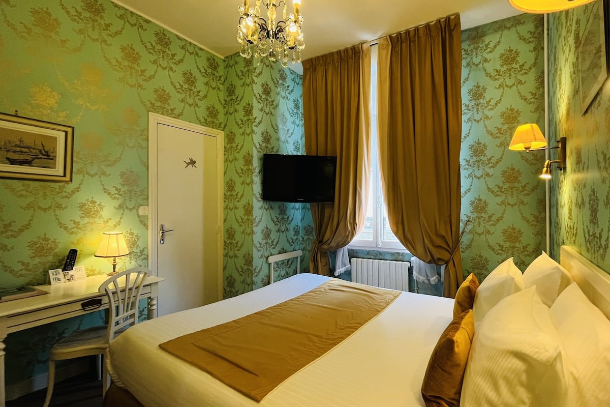 A hotel room with a bed, a desk, a chair, a television, and a window with curtains.