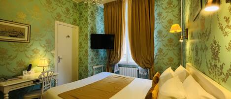 A hotel room with a bed, a desk, a chair, a television, and a window with curtains.