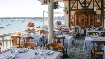 A restaurant with tables set for dining, a view of the sea, and nautical-themed decor.