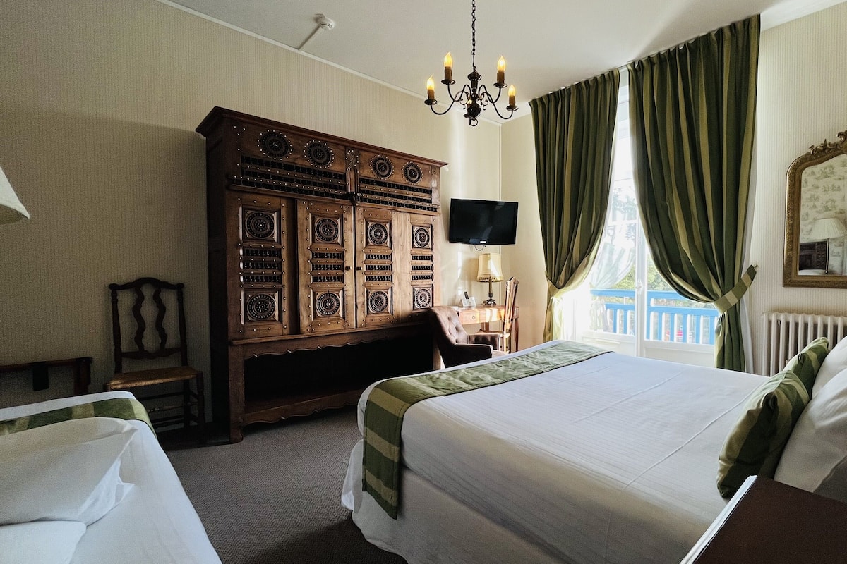 A hotel room with a large bed, a wooden wardrobe, a desk with a chair, a television, and a window with curtains.
