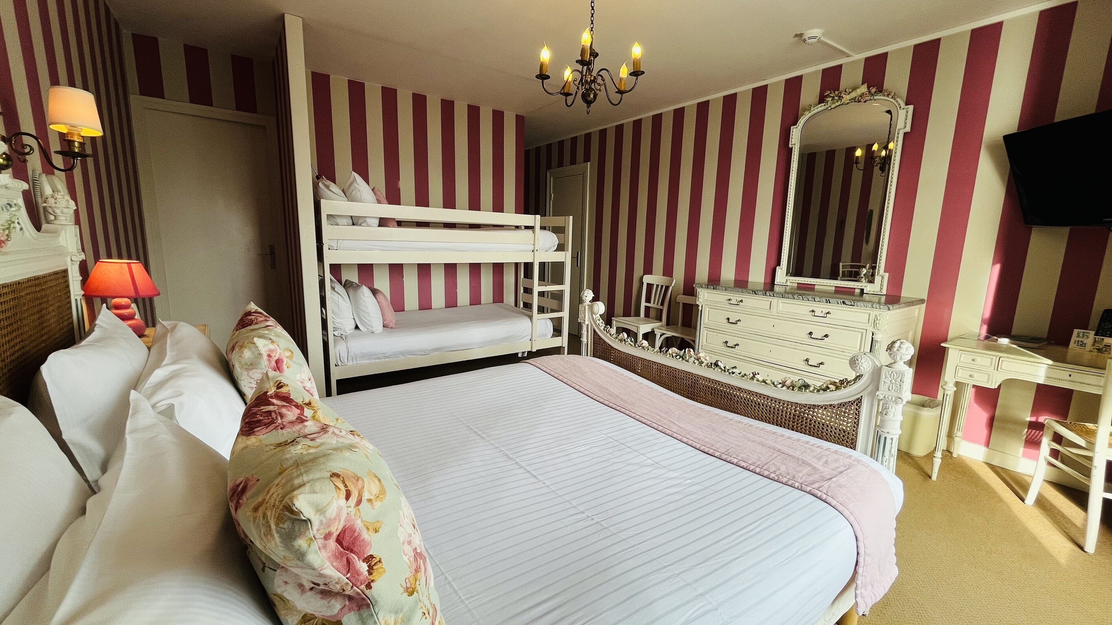 A hotel room with a bunk bed, a dresser, a vanity with a mirror, and a television on the wall.
