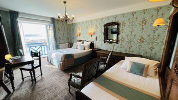 A hotel room with a bed, a desk, a chair, a dresser, and a chandelier.