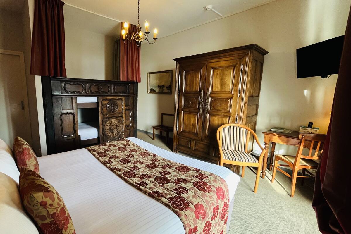 A hotel room with a large bed, a wooden wardrobe, a desk with a chair, and a television on the wall.