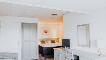 Quarto de hotel com cama, escrivaninha, cadeira, guarda-roupa e espelho.