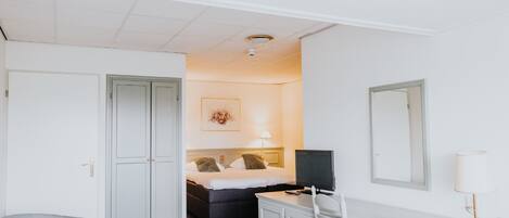 Habitación de hotel con cama, escritorio, silla, armario y espejo.
