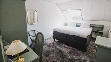 Habitación de hotel con cama, escritorio con lámpara, silla, cómoda y espejo grande.