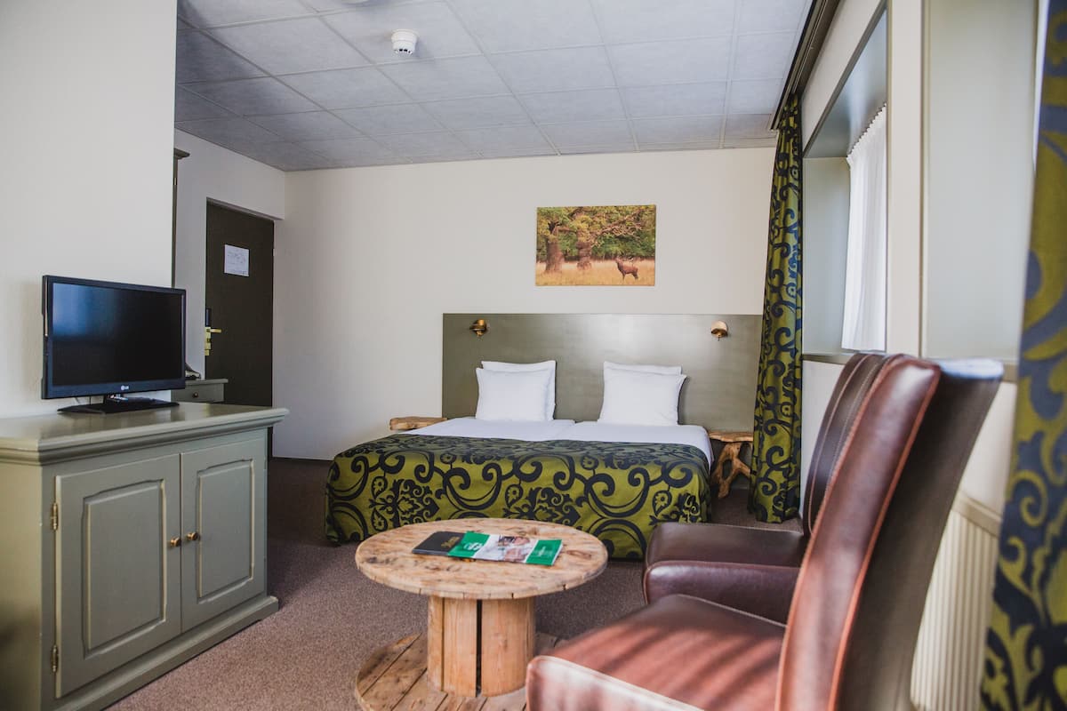 Une chambre d’hôtel avec un lit, un téléviseur posé sur un meuble, une table ronde en bois et un fauteuil en cuir.