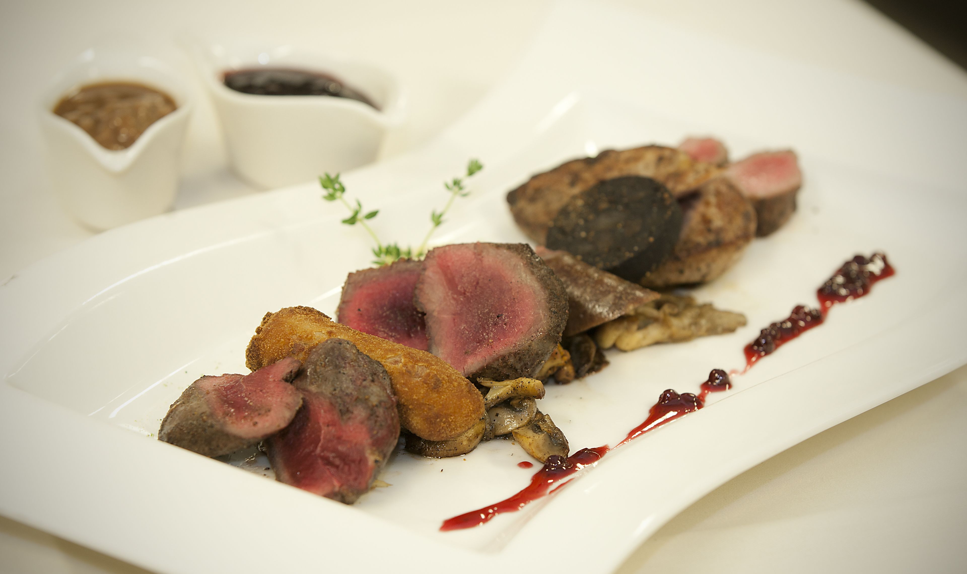 A plate of food with sliced meat and mushrooms, accompanied by small bowls of sauce.