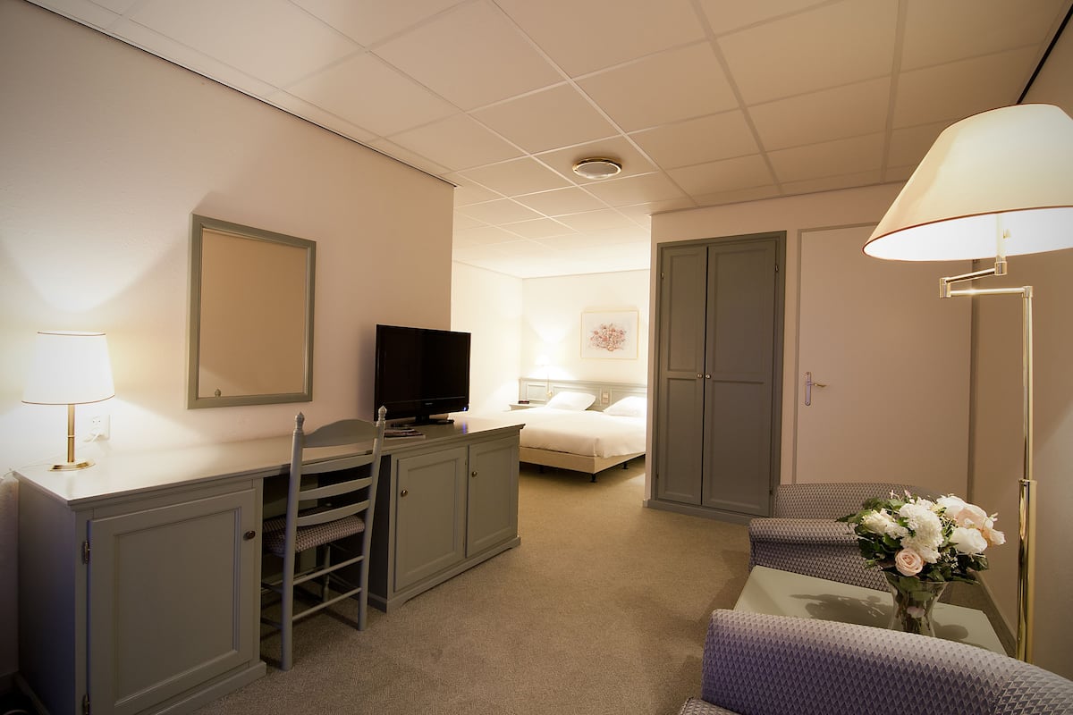 Une chambre d’hôtel avec un lit, un bureau avec une télévision, une chaise, une lampe et un vase avec des fleurs.