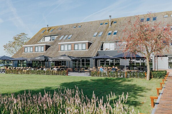 A modern building with multiple levels, outdoor seating areas, and a well-maintained lawn. - Hotel, Sportsbar & Brasserie Dorhout Mees (Biddinghuizen)