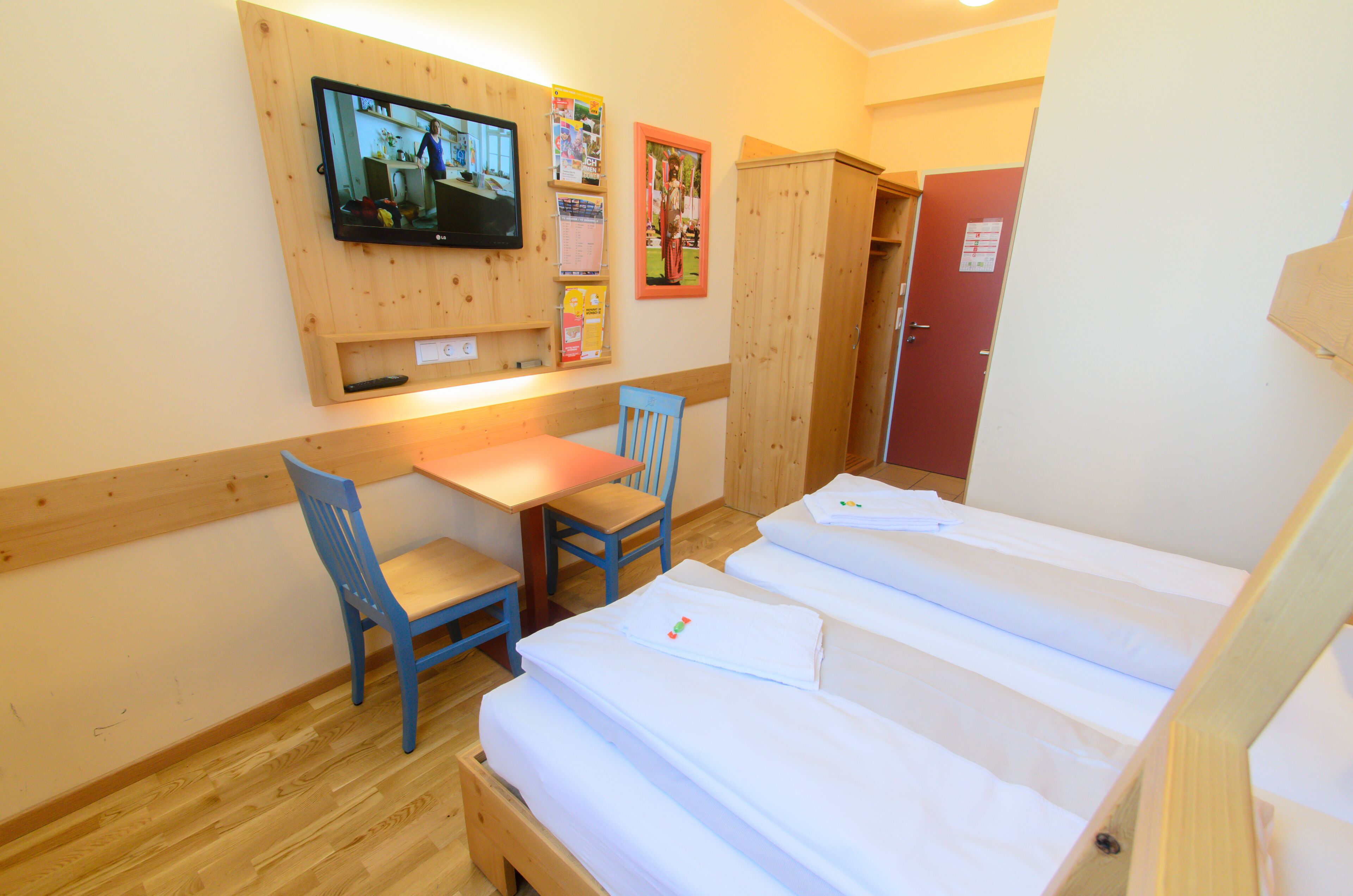 Een kamer met twee bedden, een bureau, een stoel, een televisie en een prikbord.