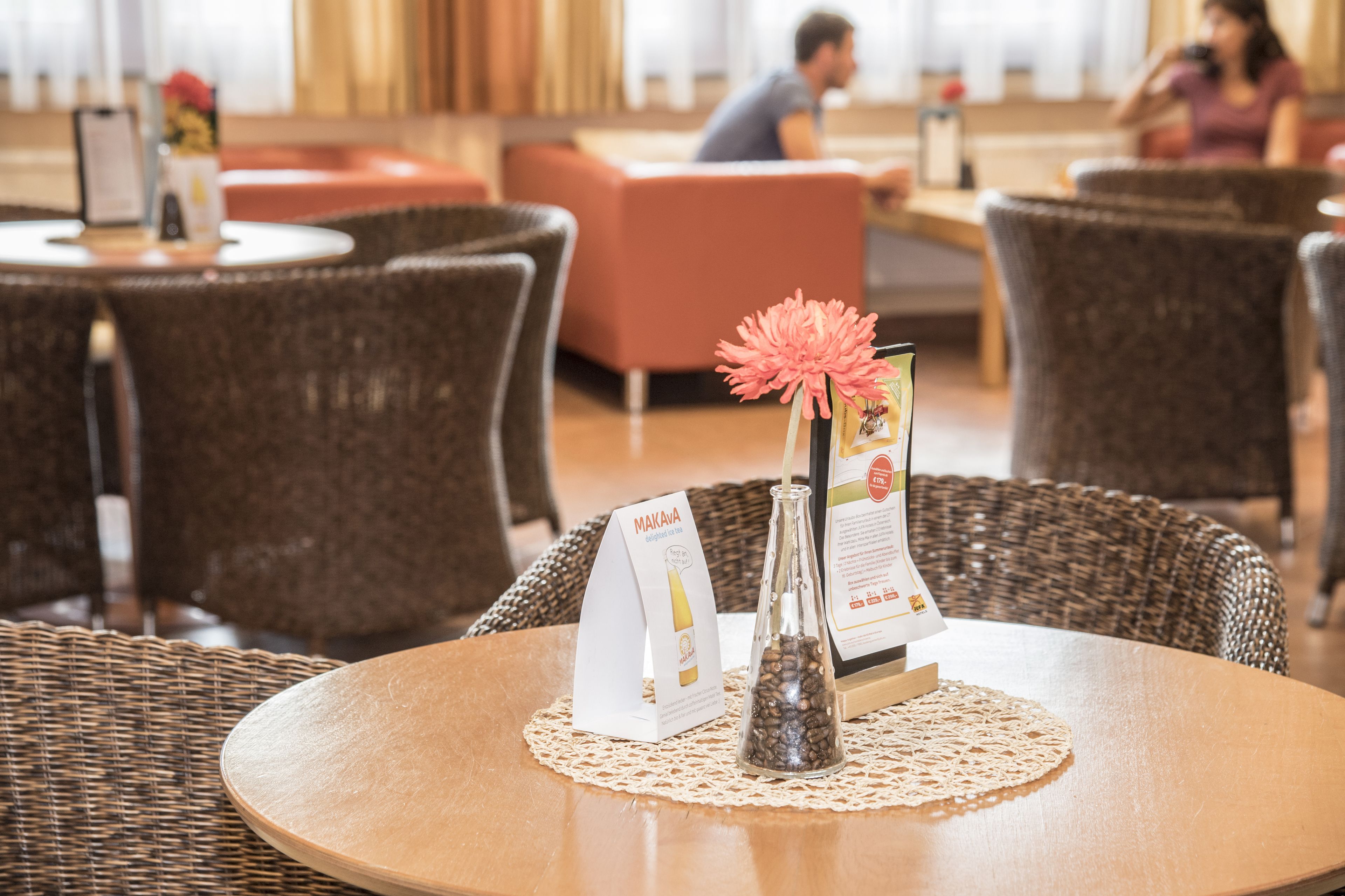Ein Restaurantambiente mit Korbstühlen und einem runden Tisch, einem Menüständer und einer dekorativen Blumenvase.