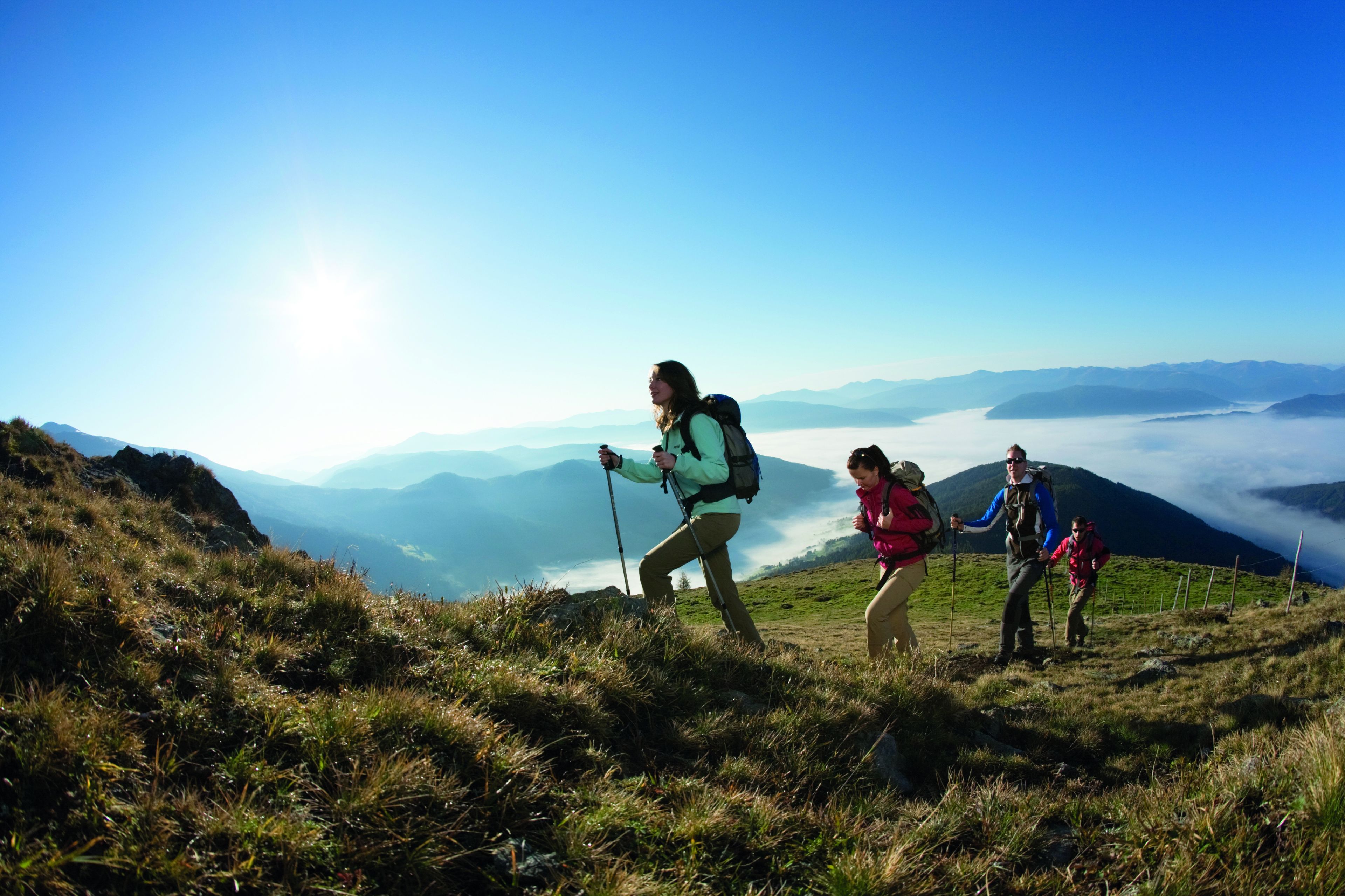 A group of hikers on a grassy mountain trail with a clear sky and distant mountains.