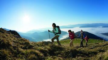A group of hikers on a grassy mountain trail with a clear sky and distant mountains.