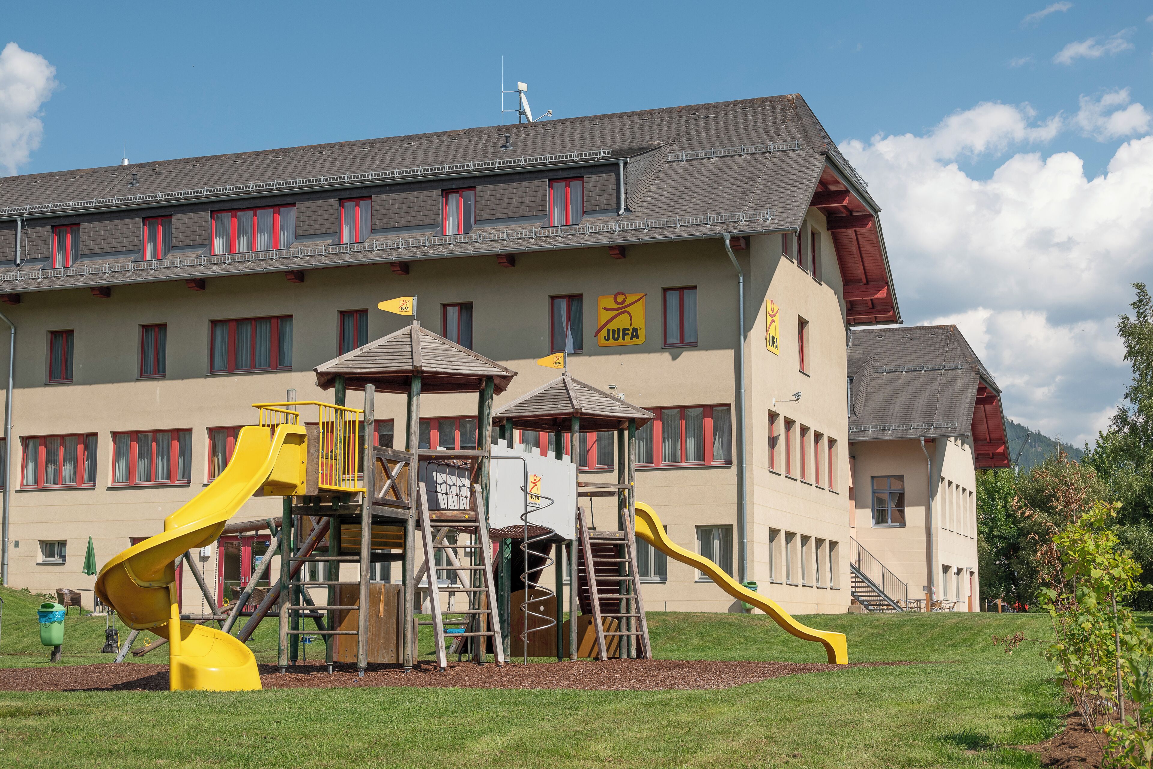 A playground with slides and climbing structures in front of a building with multiple windows and a sign.
