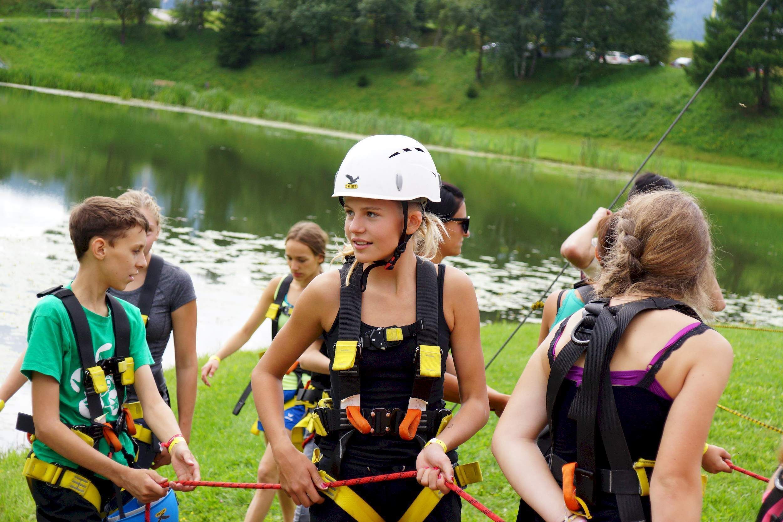 A group of people wearing safety harnesses and helmets, standing near a body of water.