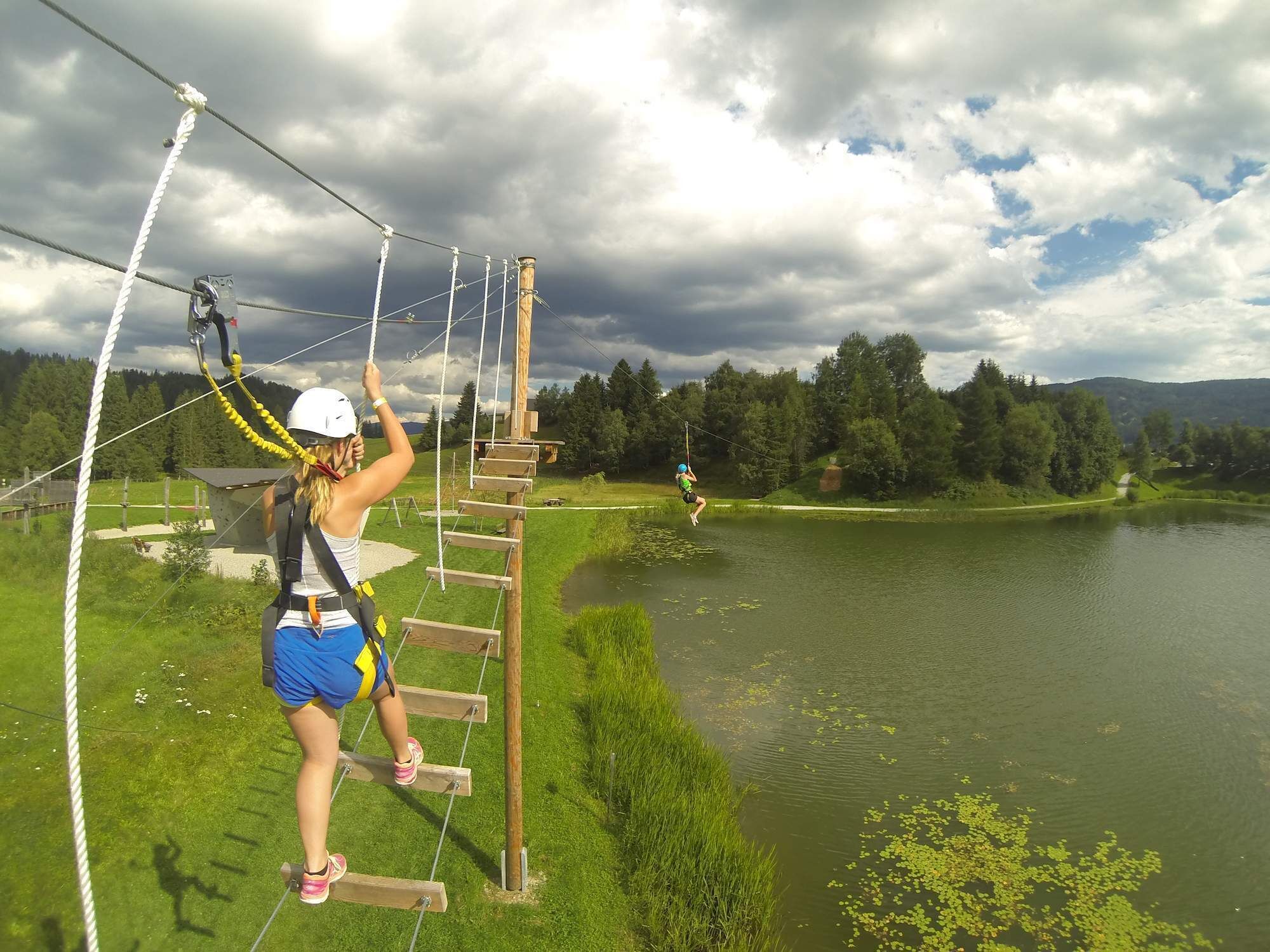 A rope bridge over a body of water with a forested landscape in the background.