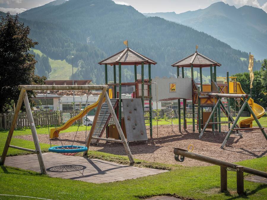 Un parque infantil con toboganes y estructuras para escalar, con montañas al fondo.