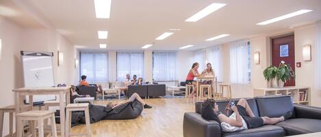 A spacious, well-lit room with a whiteboard, wooden tables, and comfortable seating areas.