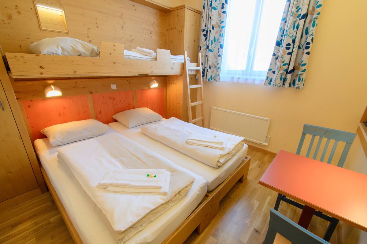 Ein Zimmer mit zwei Betten, darunter ein Holzbettkasten und ein Tisch mit einem Stuhl.