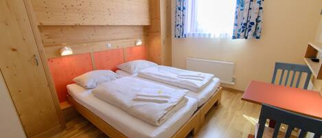 A room with a wooden bed, a small table, and a chair.