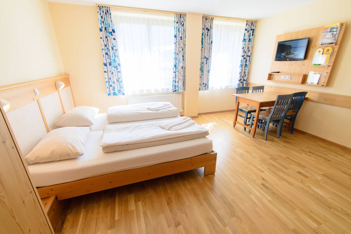 Ein Zimmer mit einem hölzernen Bett, einem Schreibtisch und einem Fernseher an der Wand.