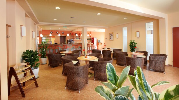 Un vestíbulo de hotel con mobiliario de mimbre, una zona de bar y plantas en macetas.