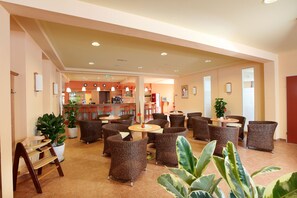 Un hall d’hôtel aménagé avec des meubles en osier, un coin bar et des plantes en pot.