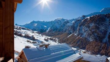 Une cabane en bois, dont le toit est recouvert de neige, entourée de montagnes enneigées et sous un ciel dégagé.
