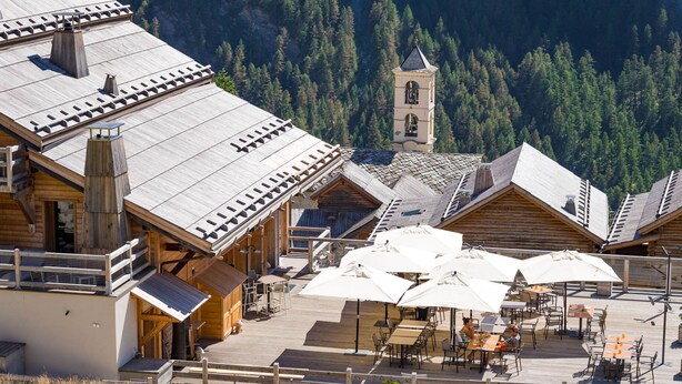 A wooden chalet with a dining area and outdoor seating, surrounded by forested mountains. - Hotel & Spa L'Alta Peyra (Saint-Veran)