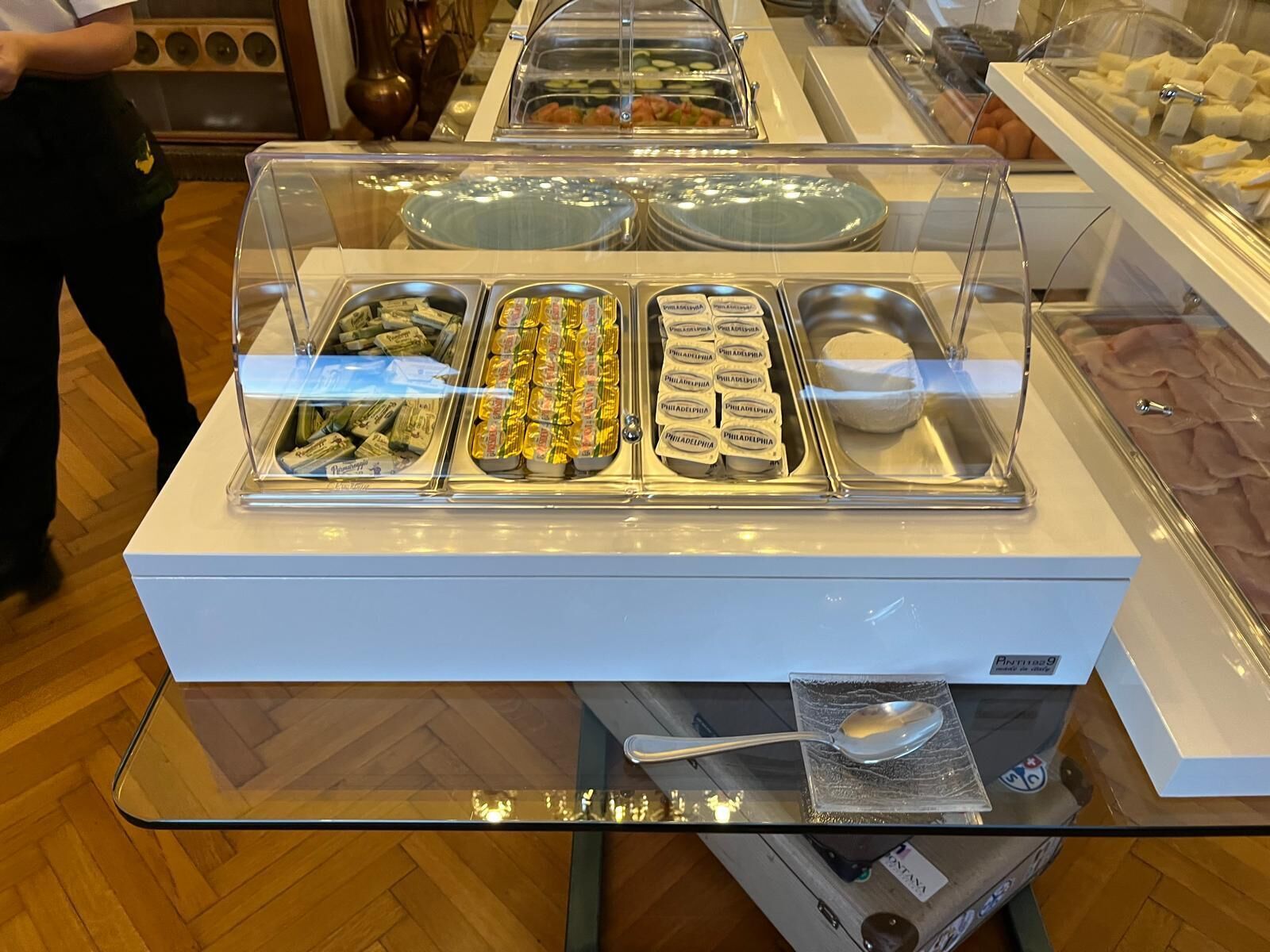 A buffet with various food items and a spoon on a glass table.