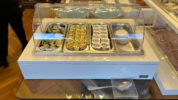 A buffet with various food items and a spoon on a glass table.