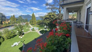 Un balcón con vistas a un jardín cuidado, una piscina y una montaña al fondo.