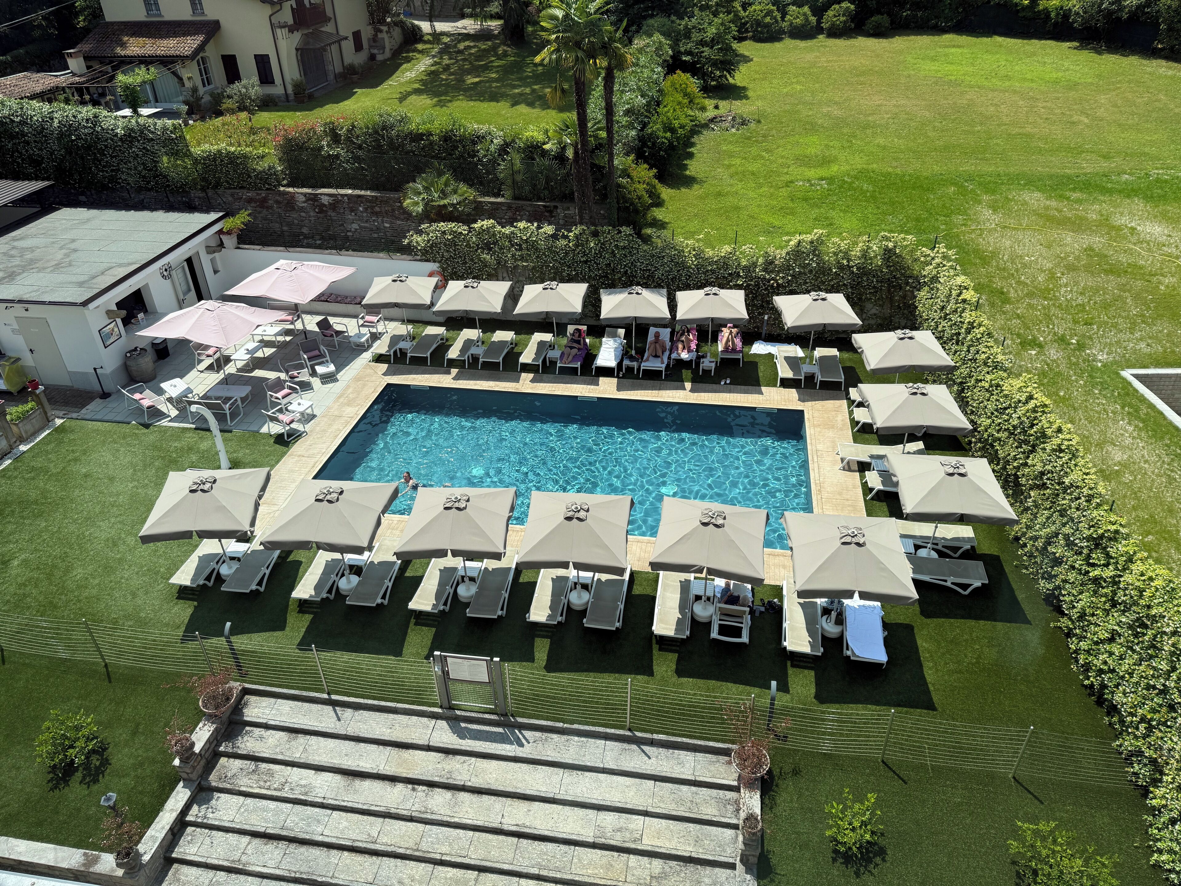 Una piscina rectangular rodeada de sillas de descanso y sombrillas, con una escalera de piedra que baja.
