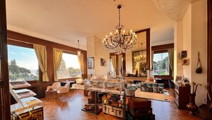 Una habitación amplia con suelo de madera, un candelabro, una zona de buffet y ventanas grandes con vistas.