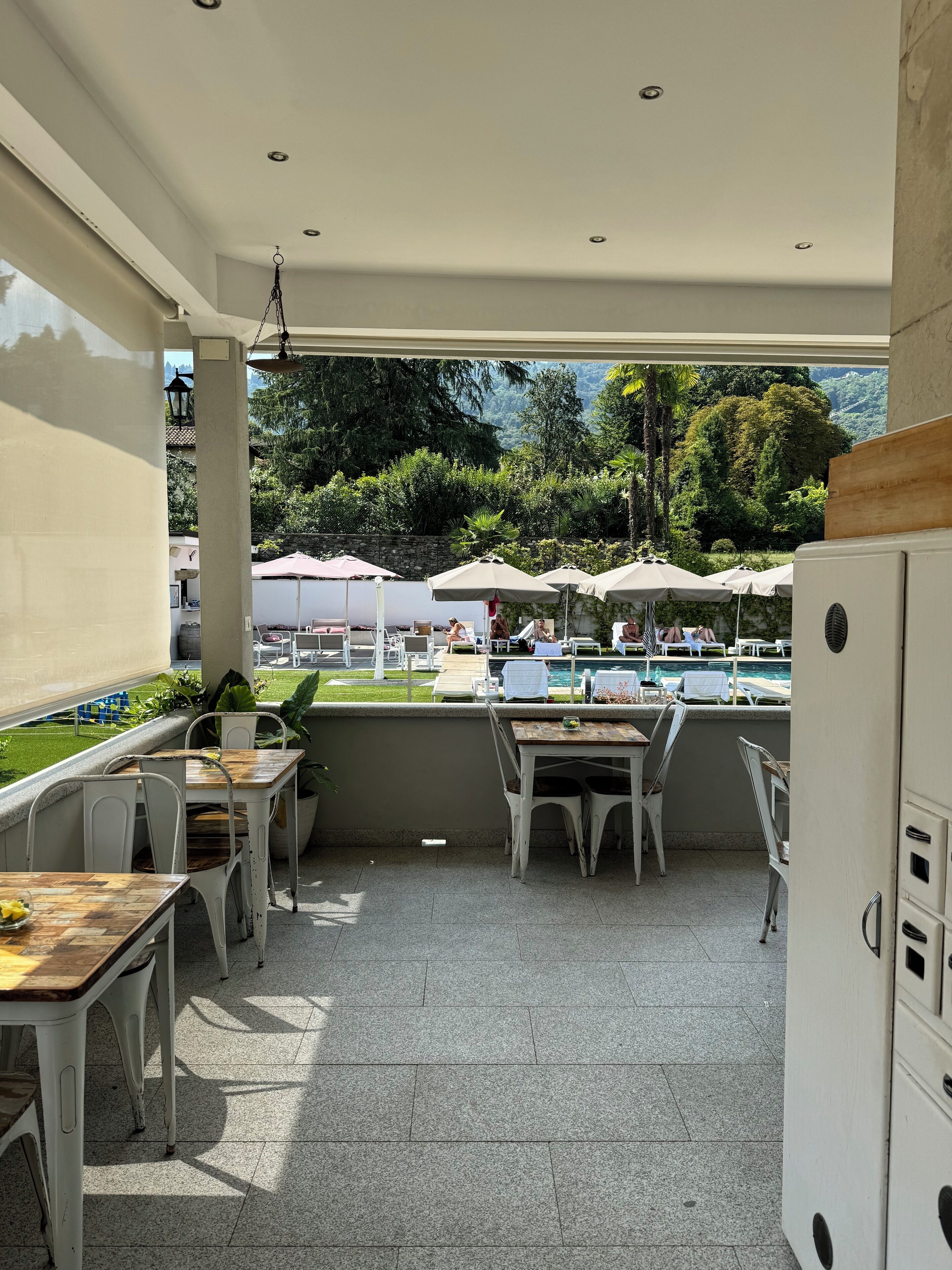 Un patio al aire libre con mesas y sillas, una piscina y vistas a zonas verdes y montañas.